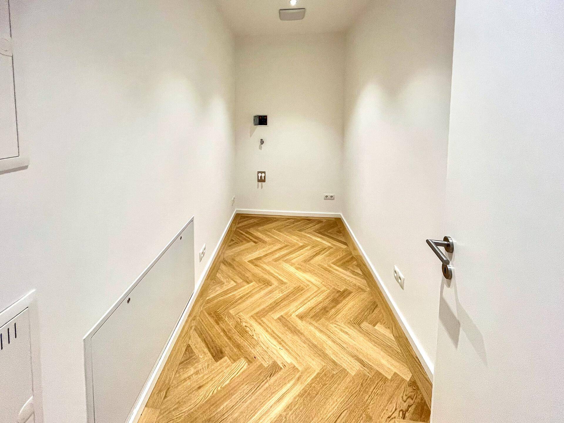 Schmaler Hauswirtschaftsraum mit Fischgrätparkett und weißen Wänden, ideal für Lagerung oder Technik.