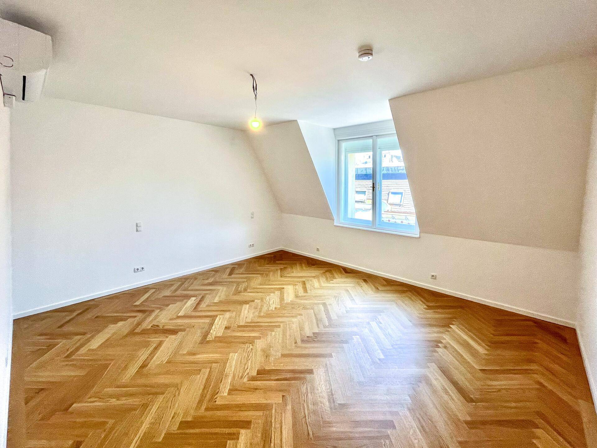 Gemütliches Schlafzimmer mit Fischgrätparkett, Dachschrägen und einem Fenster, ausgestattet mit Klimaanlage.