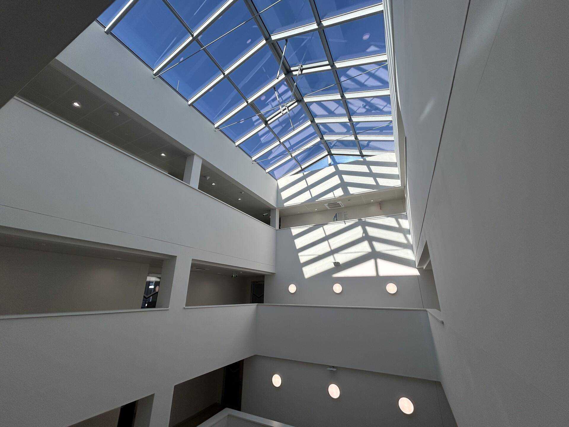 Modernes Atrium mit beeindruckendem Glasdach, das viel natürliches Licht in das Gebäude bringt.