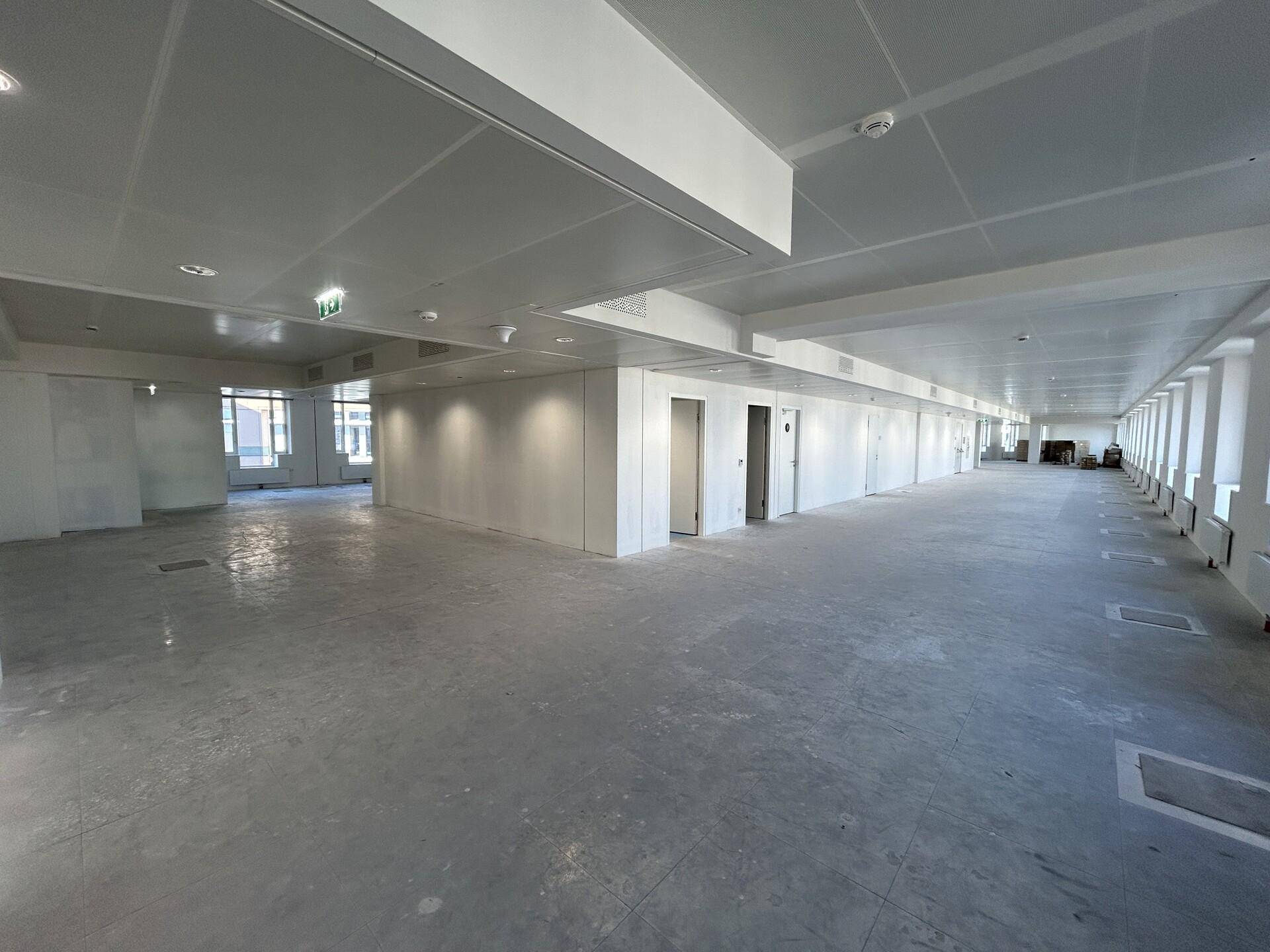Weitläufiger, unmöblierter Bürobereich mit vielen Fenstern und einer modernen, hellen Deckenkonstruktion.