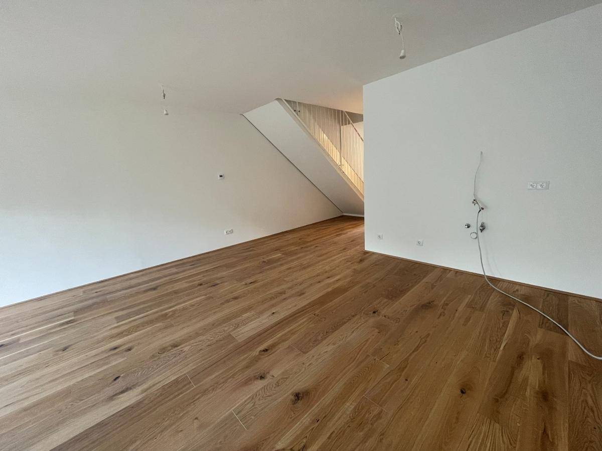 Heller Raum mit Holzboden und Treppenaufgang, ideal für einen offenen Wohnbereich.