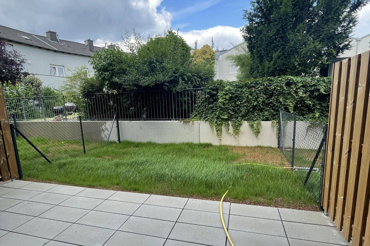 Kleiner privater Gartenbereich mit Rasenfläche und gepflasterter Terrasse hinter einem Zaun.