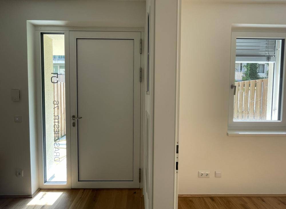 Heller Eingangsbereich mit Holzboden und einer modernen weißen Tür.