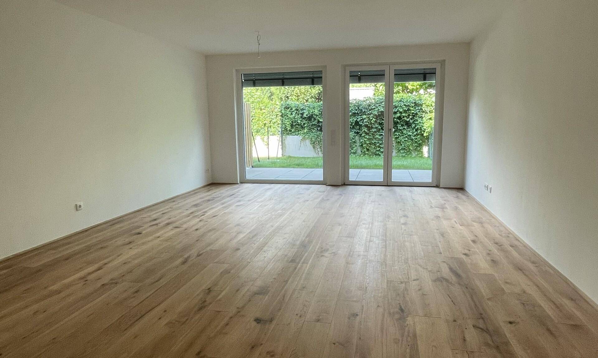 Geräumiges Wohnzimmer mit Holzboden und großen Fenstern zum Garten.