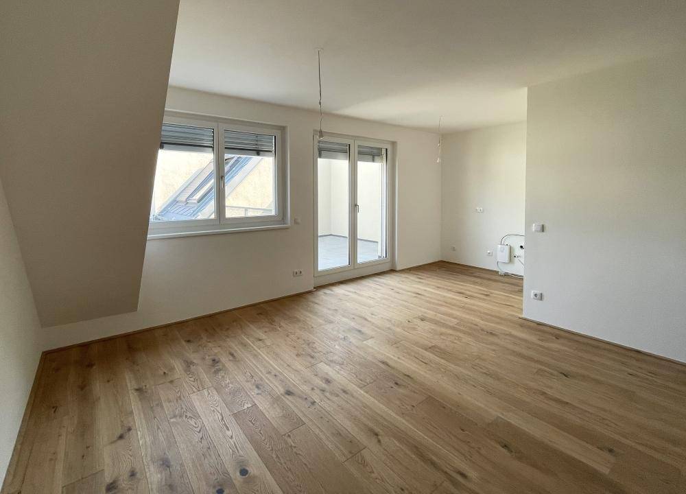 Helles Zimmer mit Holzboden, Dachschräge und Zugang zu einem Balkon.