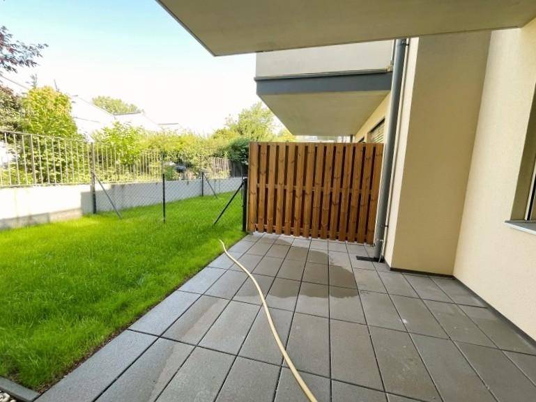 Sonniger Terrassenbereich mit gepflastertem Boden und privatem Gartenanteil, umgeben von einem Holzzaun.