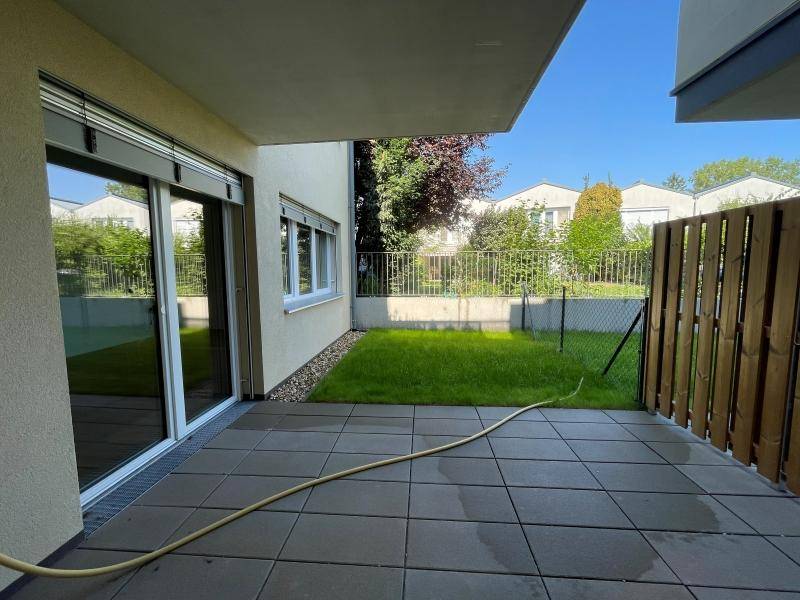 Helle Terrasse mit direktem Zugang zum privaten Garten und Blick auf die umliegende Wohnbebauung.