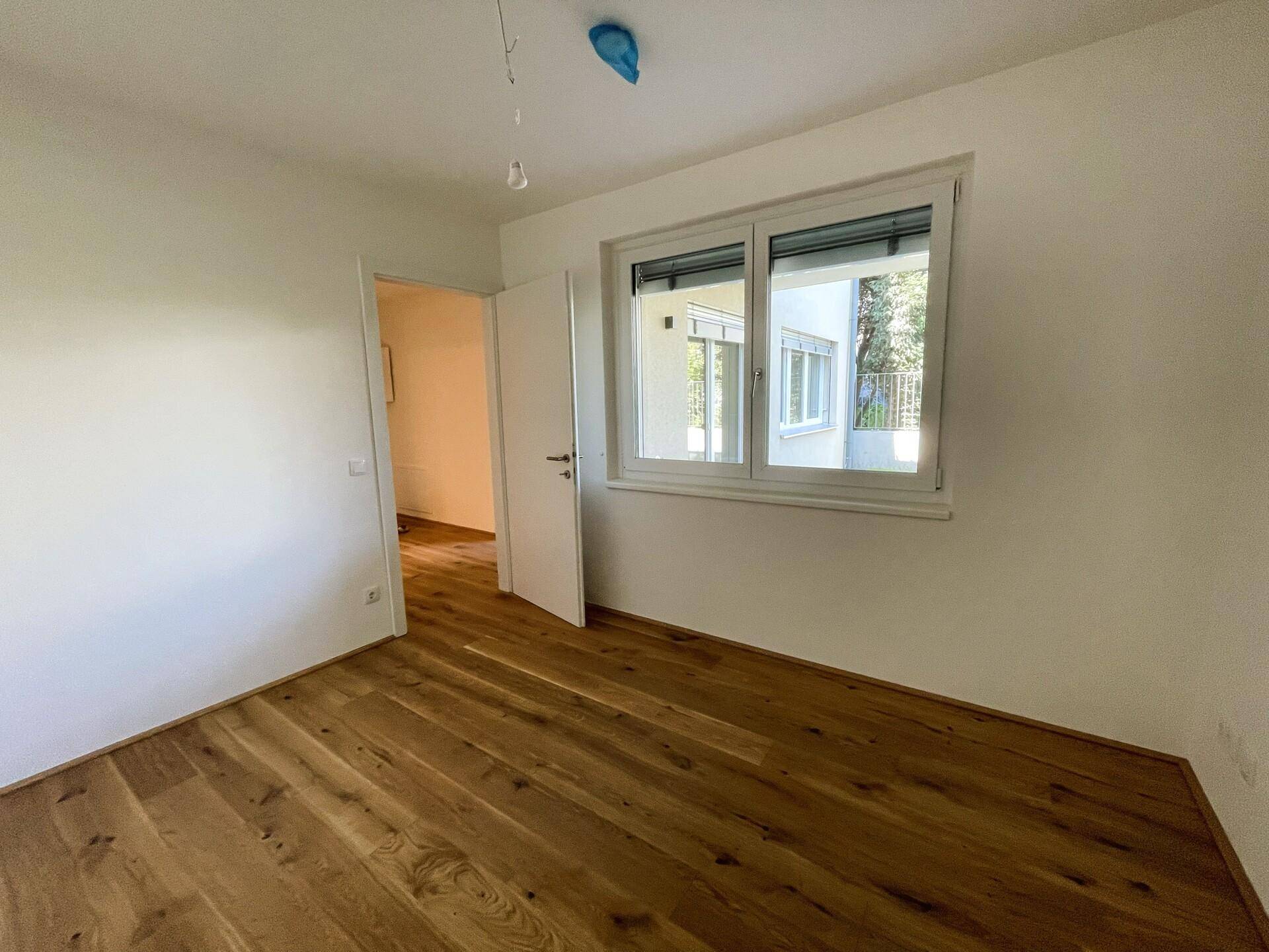Ruhiges Schlafzimmer mit Eichenparkett und großem Fenster, das eine angenehme Wohnatmosphäre schafft.