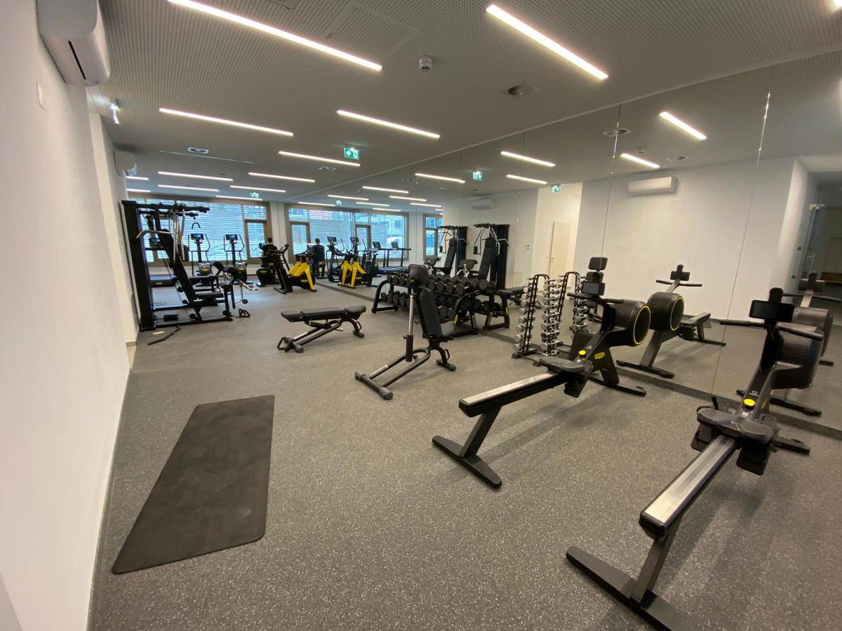 Gut ausgestatteter Fitnessraum mit verschiedenen Trainingsgeräten und Spiegelflächen.