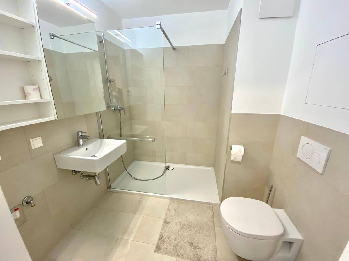 Modernes Badezimmer mit begehbarer Dusche, Wand-WC und hellen Fliesen.