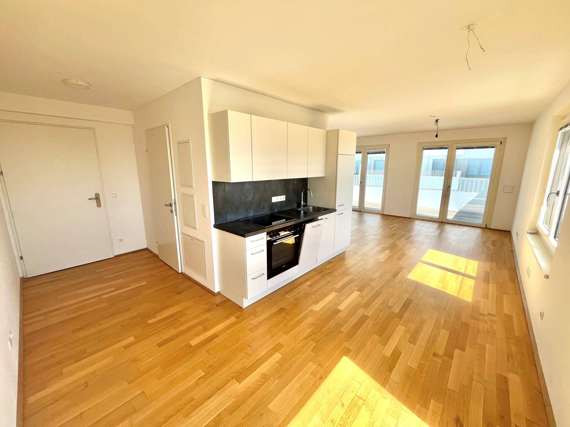 Lichtdurchfluteter Wohnbereich mit Parkettboden, moderner Küchenzeile und Balkonzugang.