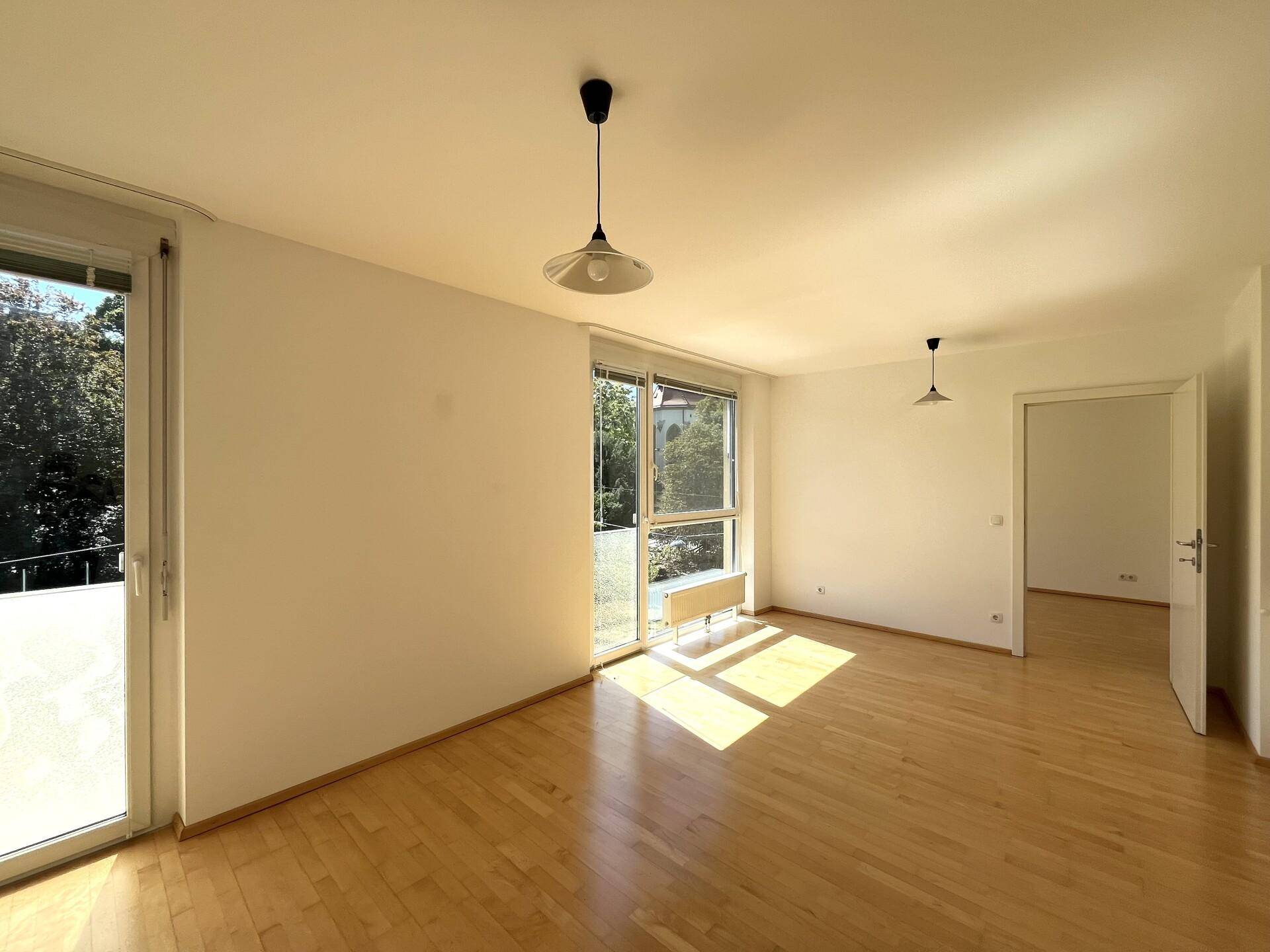 Lichtdurchflutetes Wohnzimmer mit Parkettboden und großen Fenstern, die viel Sonnenlicht hereinlassen.