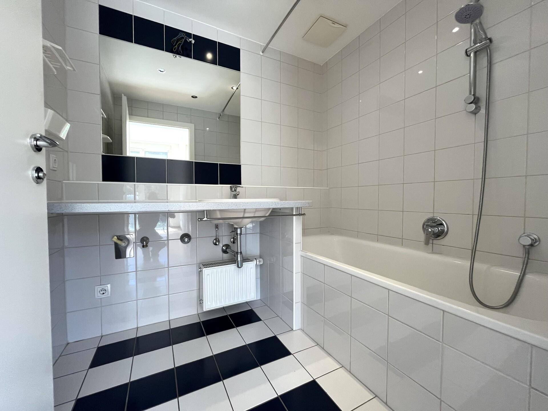 Badezimmer mit Badewanne, Waschbecken, Spiegel und markanten schwarz-weißen Fliesen.