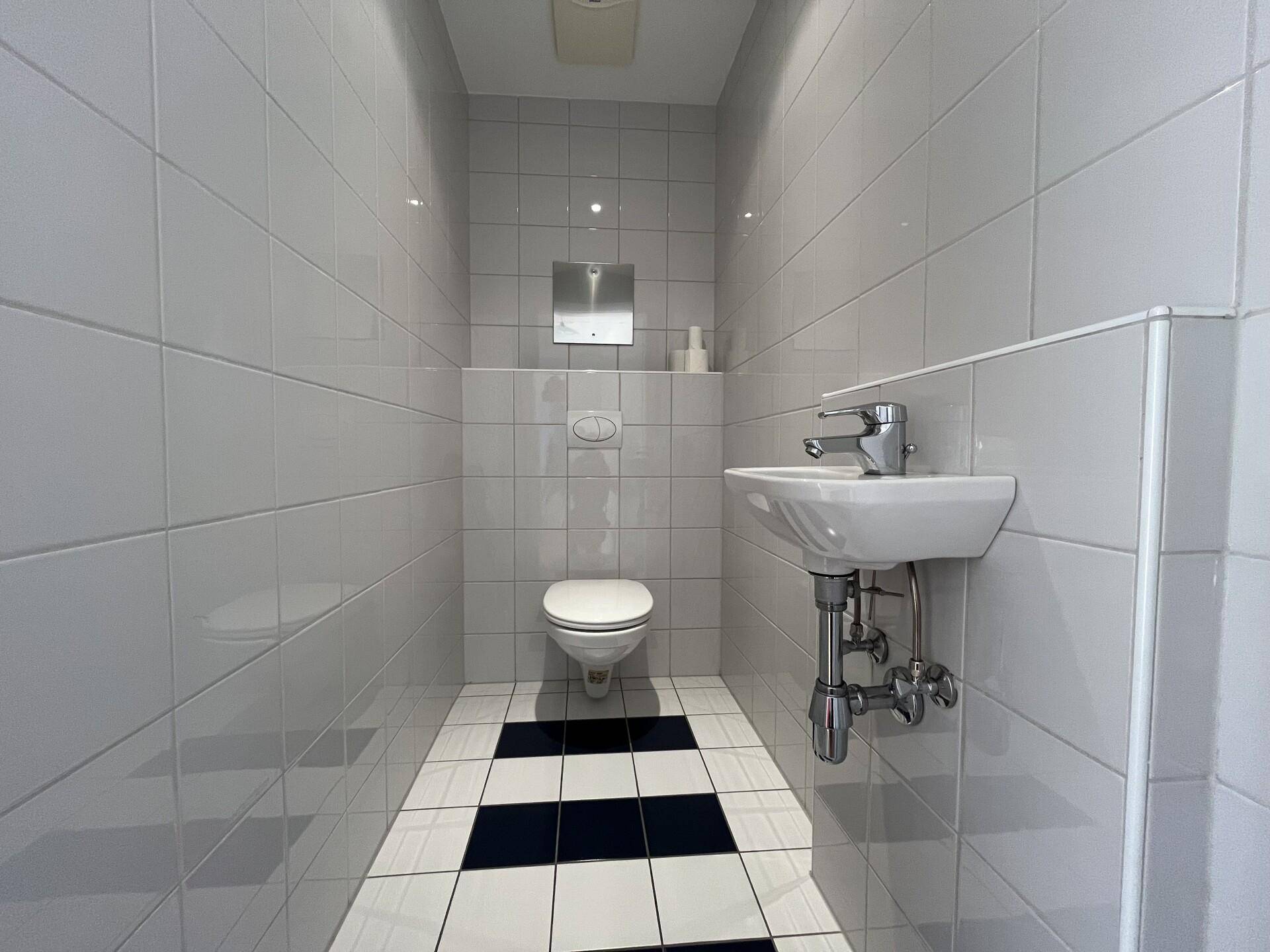 Separates WC mit Toilette, kleinem Waschbecken und schwarz-weißen Bodenfliesen.