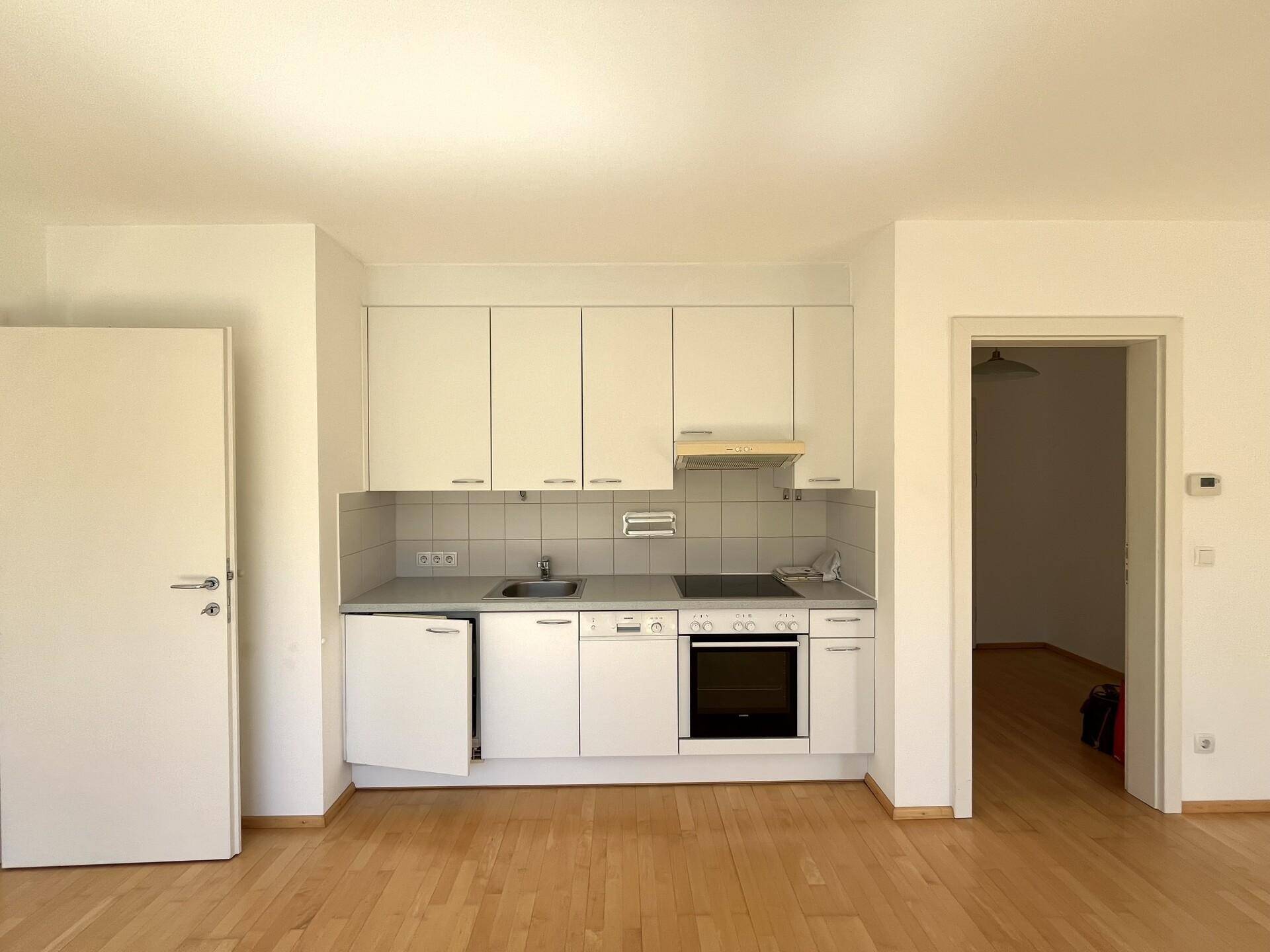 Funktionale Einbauküche mit weißen Schränken, Herd, Backofen und Spülmaschine.