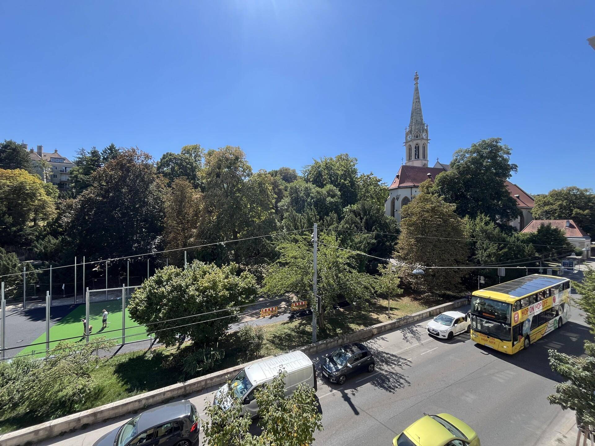 Blick auf die Straße, umliegende Bäume, eine Kirche und einen Sportplatz.