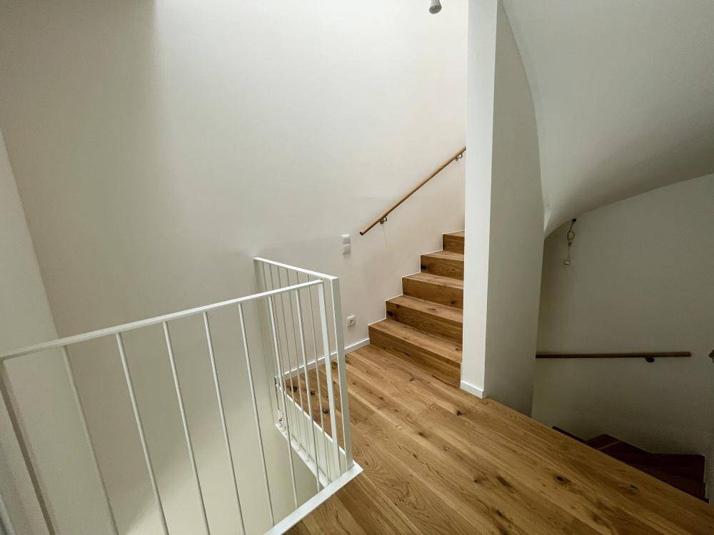 Moderne Holztreppe mit weißem Geländer, die die verschiedenen Ebenen des Hauses verbindet.