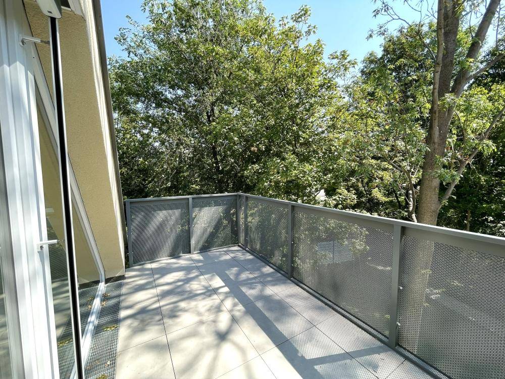 Heller Balkon mit modernen Fliesen und Metallgeländer, umgeben von üppigem Grün.