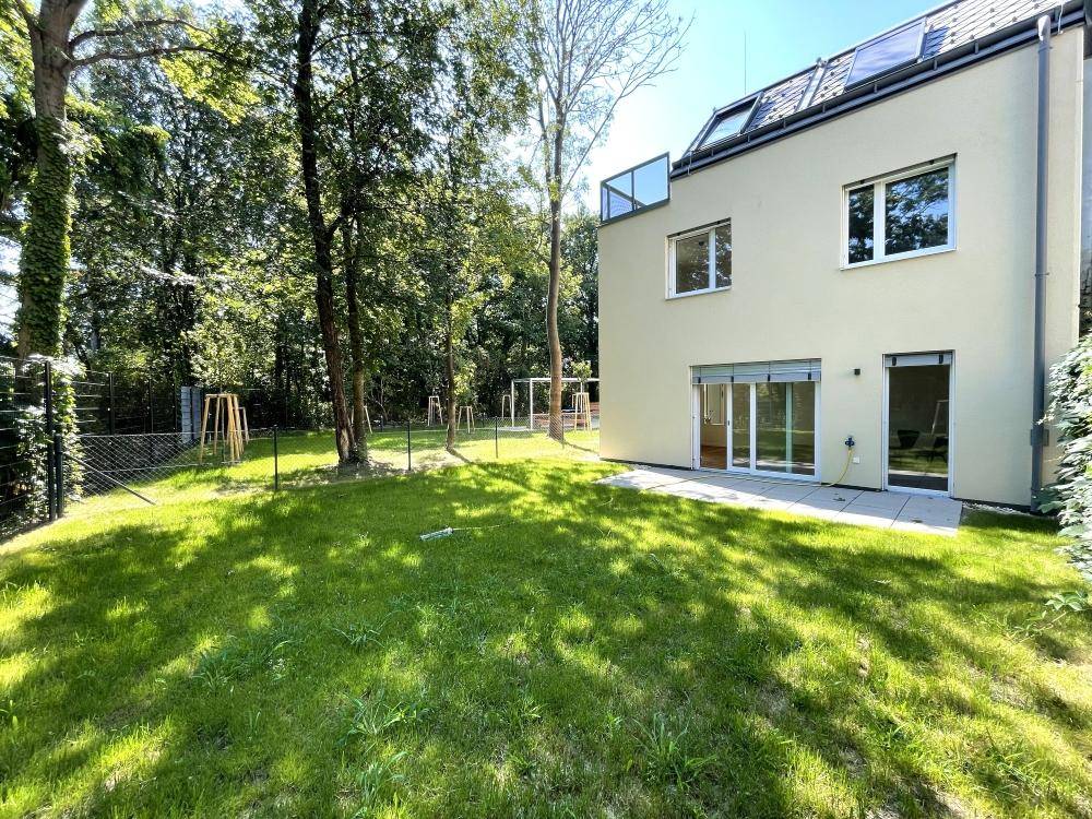 Sonniger Terrassenbereich mit direktem Zugang zum gepflegten Rasen und umgebenden Bäumen.