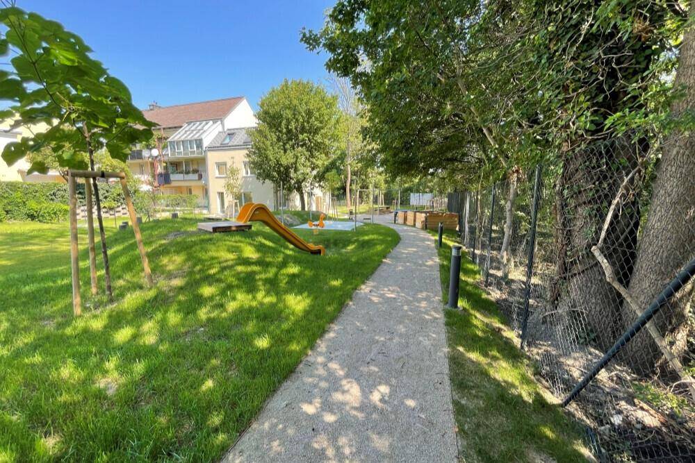 Geschwungener Weg durch den Gemeinschaftsgarten mit Spielgeräten und Bäumen.