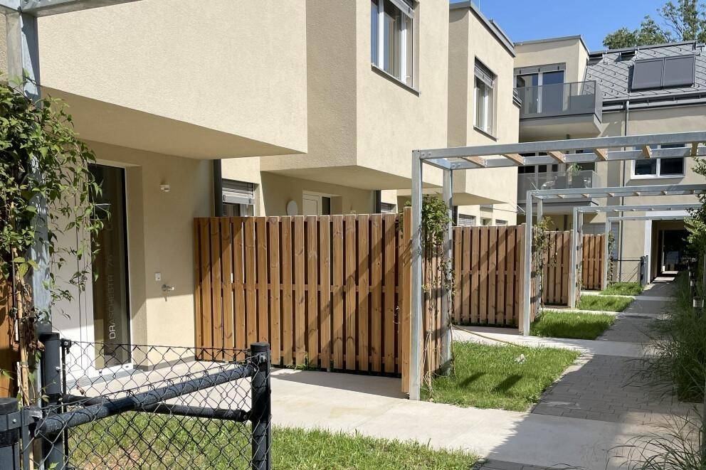 Private Gartenbereiche mit Holzzäunen und Pergolen vor modernen Reihenhäusern.