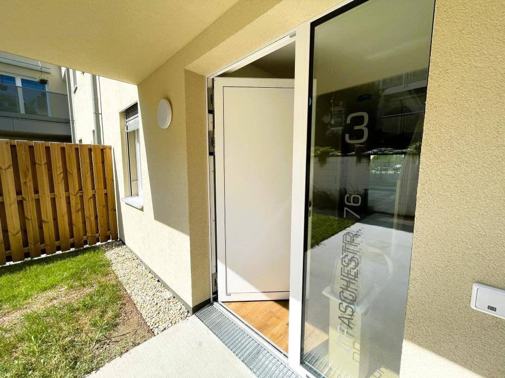Eingangsbereich eines modernen Reihenhauses mit Glastür und kleinem Vorgarten.