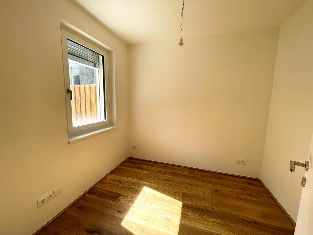 Leeres Zimmer mit Eichenparkettboden und einem Fenster, das viel Tageslicht hereinlässt.