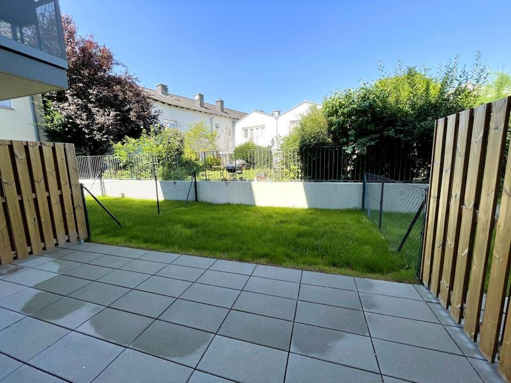 Privater Gartenbereich mit gepflasterter Terrasse und Rasenfläche, umgeben von einem Zaun.