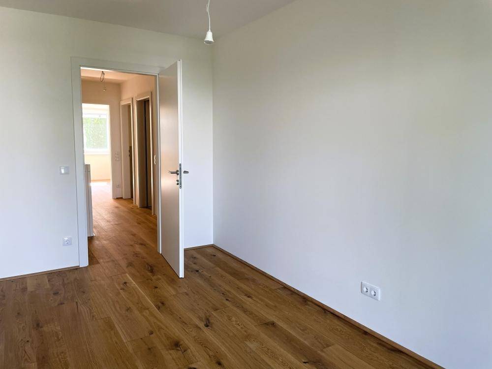 Helles, leeres Zimmer mit Eichenparkettboden und weiß gestrichenen Wänden.