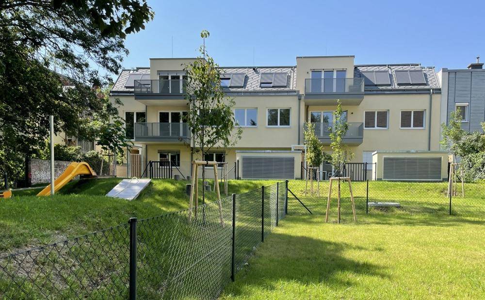 Gemeinschaftsgarten mit Rutsche und viel Grünfläche hinter den modernen Gebäuden.
