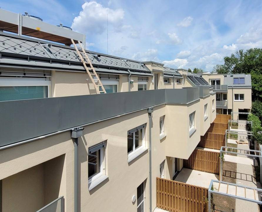 Obere Etagen des Gebäudes mit modernen Balkonen und Dachdetails unter blauem Himmel.