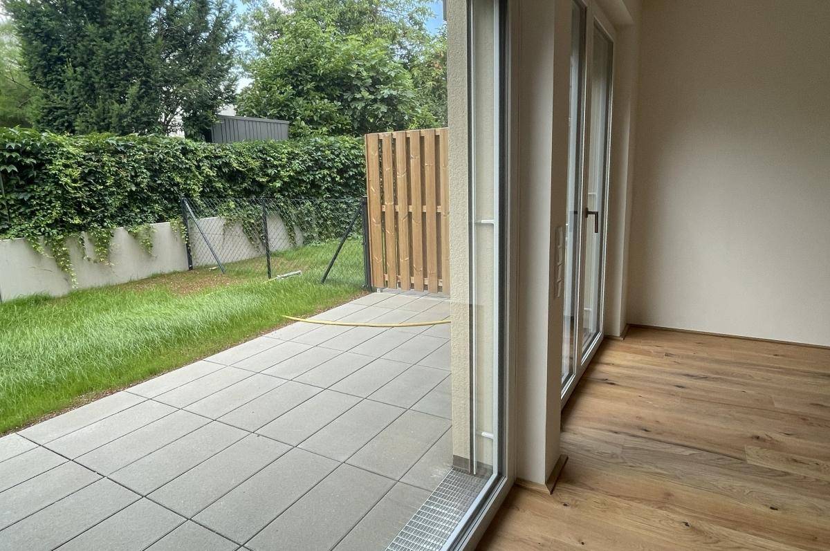 Heller Raum mit Holzboden und Zugang zu einer gepflasterten Terrasse und einem kleinen Garten.