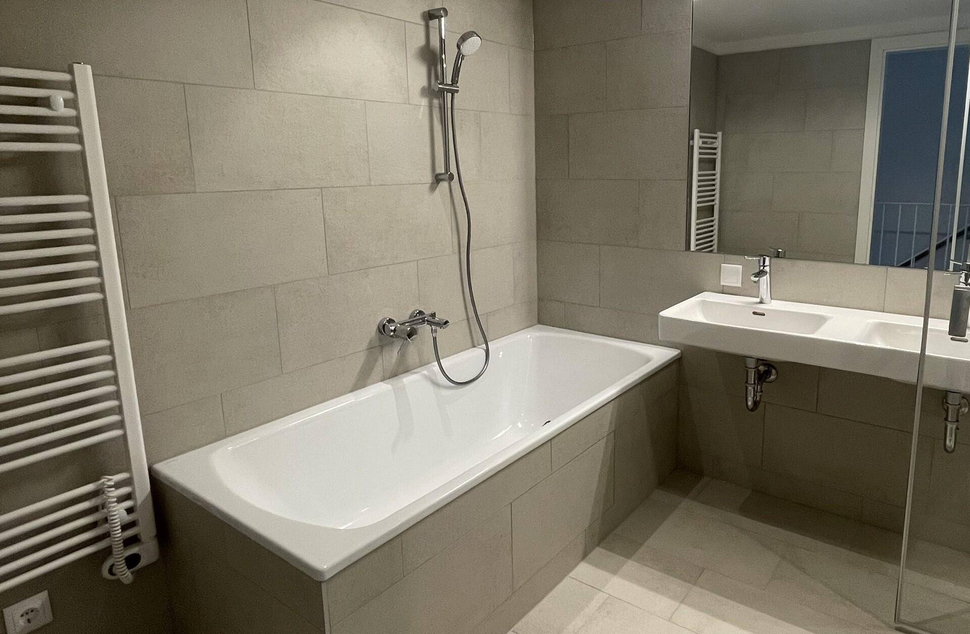 Modernes Badezimmer mit Badewanne, Waschbecken und großen Fliesen an Wänden und Boden.