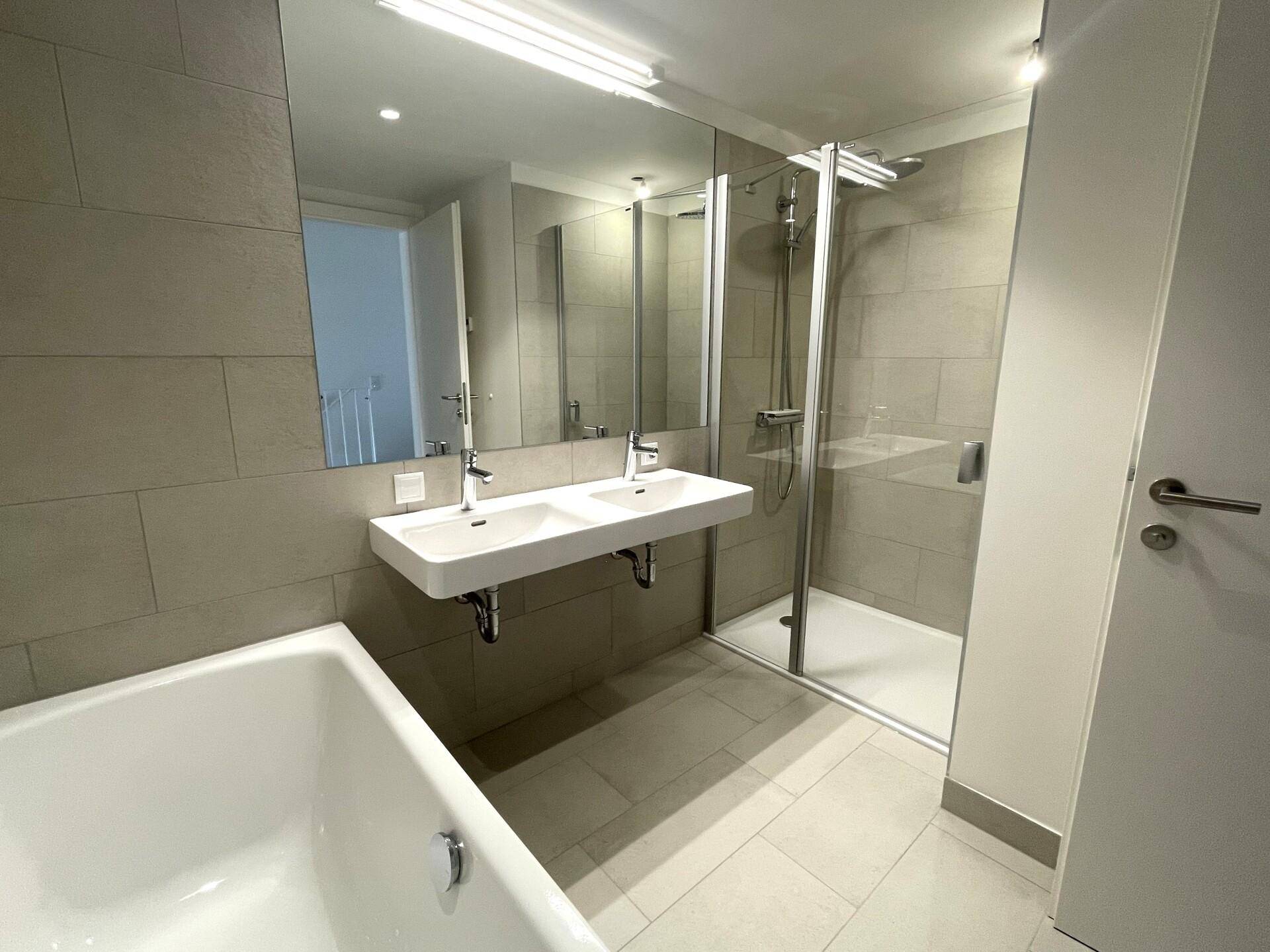 Modernes Badezimmer mit Doppelwaschbecken, großer Spiegelfläche und begehbarer Dusche.