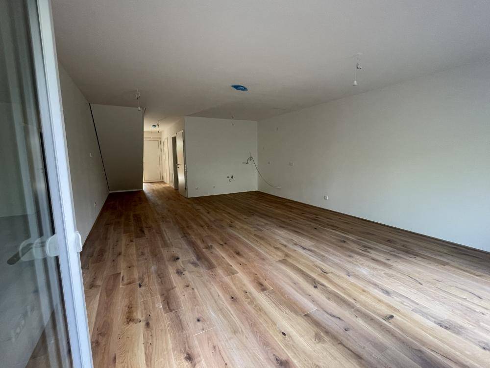 Geräumiger Wohnbereich mit Holzboden und großen Fenstern, die den Raum erhellen.