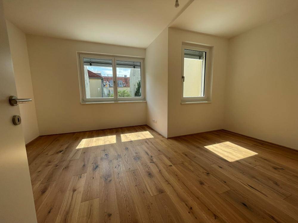 Helles Schlafzimmer mit Holzboden und zwei Fenstern, die viel Tageslicht hereinlassen.