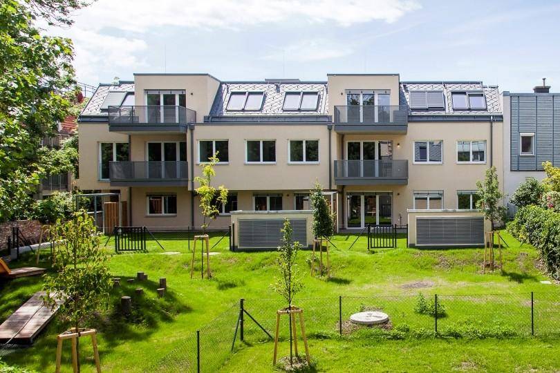 Moderne Wohngebäude mit Balkonen und einem weitläufigen, grünen Gemeinschaftsgarten mit Spielgeräten.