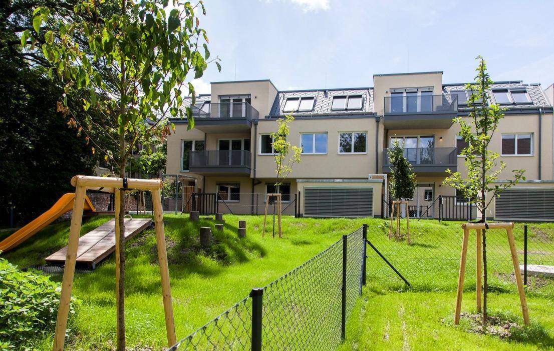 Neubauwohnungen mit Balkonen und einem weitläufigen, grünen Gemeinschaftsgarten mit Spielgeräten.