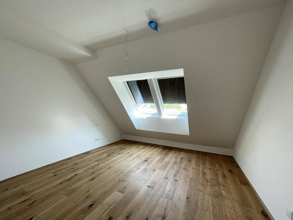 Helles Schlafzimmer im Dachgeschoss mit Holzboden und Dachfenster, bietet eine gemütliche Atmosphäre.