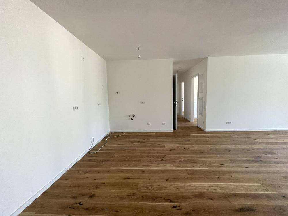 Heller, leerer Raum mit neuem Holzparkett und weißen Wänden, bereit für die Einrichtung.