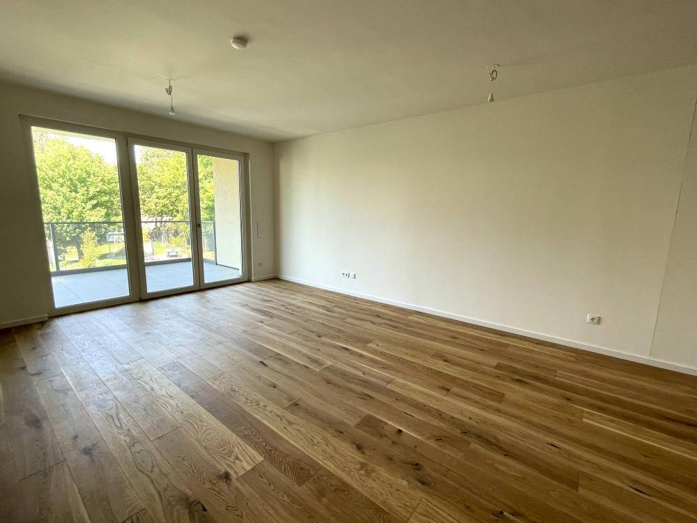 Lichtdurchfluteter Wohnbereich mit Eichenparkett und großzügigem Zugang zum Balkon.
