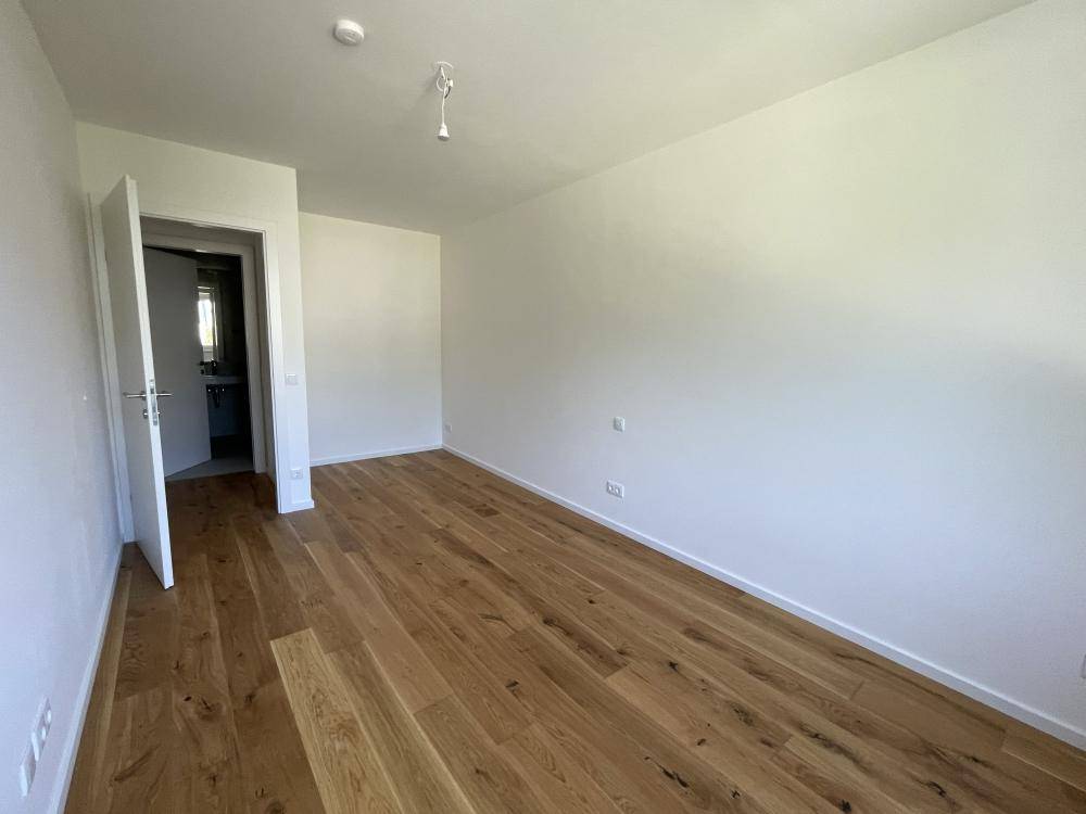 Geräumiges Schlafzimmer mit Holzparkett und Zugang zu einem weiteren Raum, möglicherweise einem Bad.