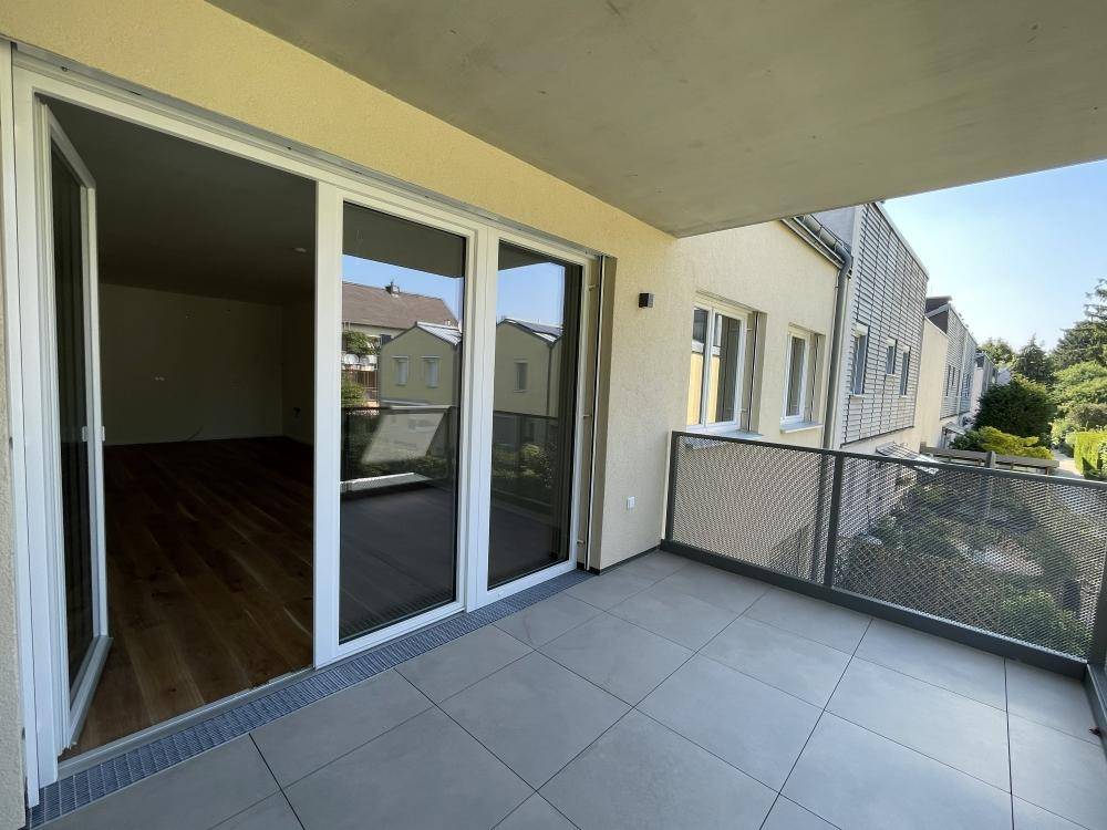 Heller Balkon mit Zugang zu einem Innenraum mit Holzparkett und großen Schiebetüren.