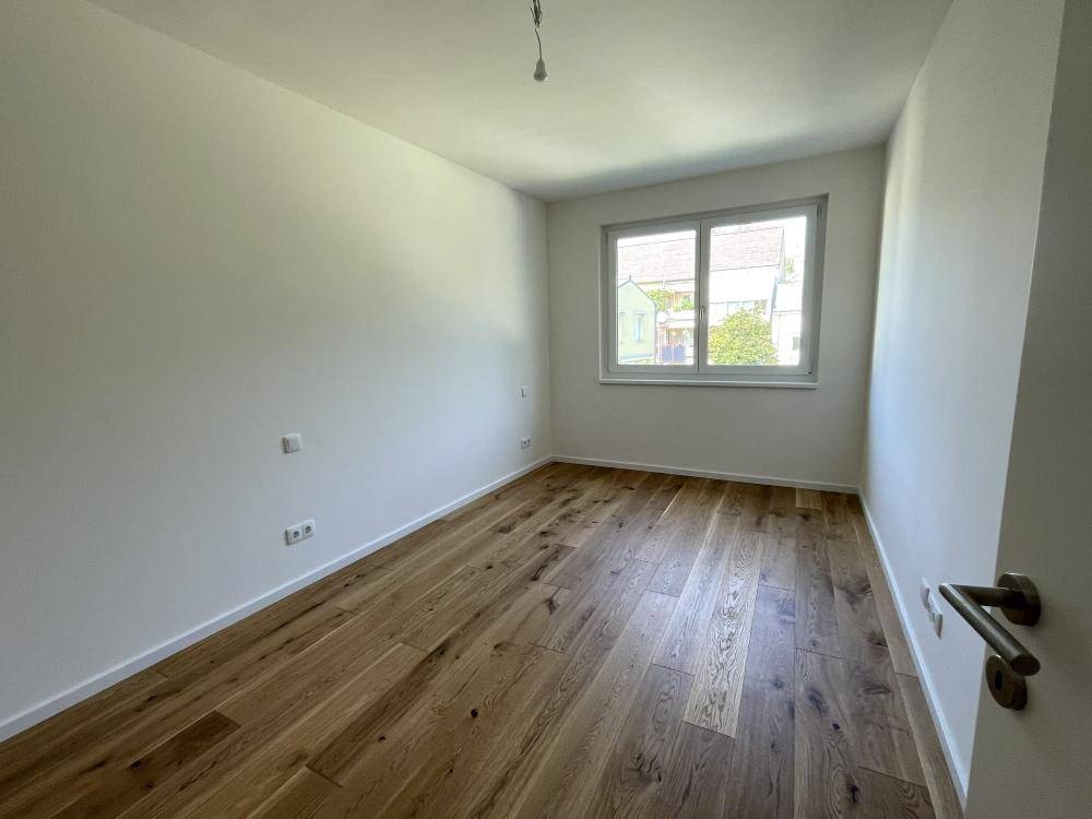 Helles Schlafzimmer mit Holzparkett und einem Fenster, das viel Tageslicht hereinlässt.