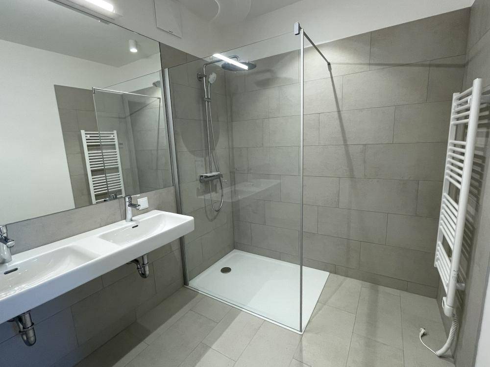 Modernes Badezimmer mit Doppelwaschbecken, großer begehbarer Dusche und Handtuchheizkörper.