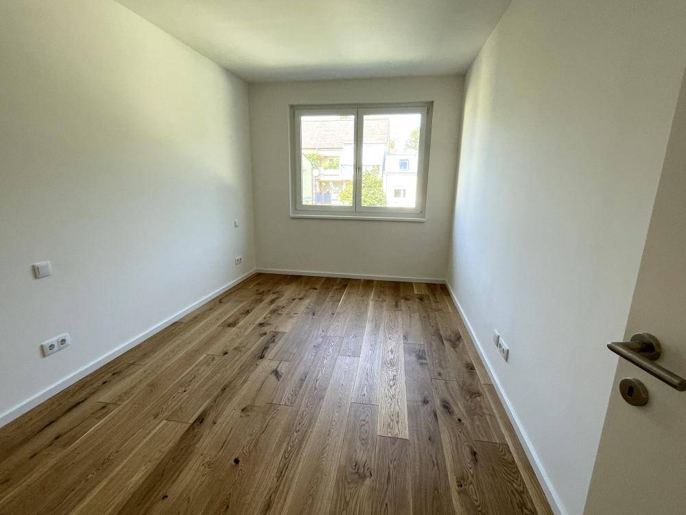 Freundliches Schlafzimmer mit Holzparkett und einem großen Fenster für natürliche Belichtung.