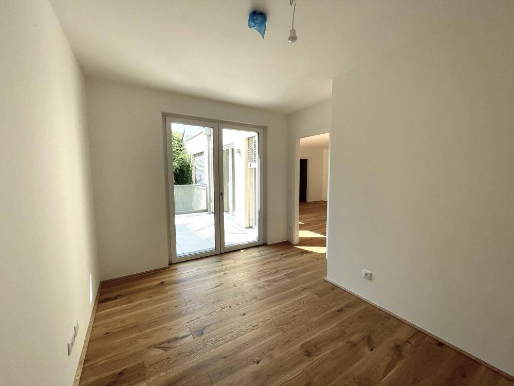 Helles Zimmer mit Holzparkett und Zugang zu einem kleinen Außenbereich, ideal als Schlafzimmer.