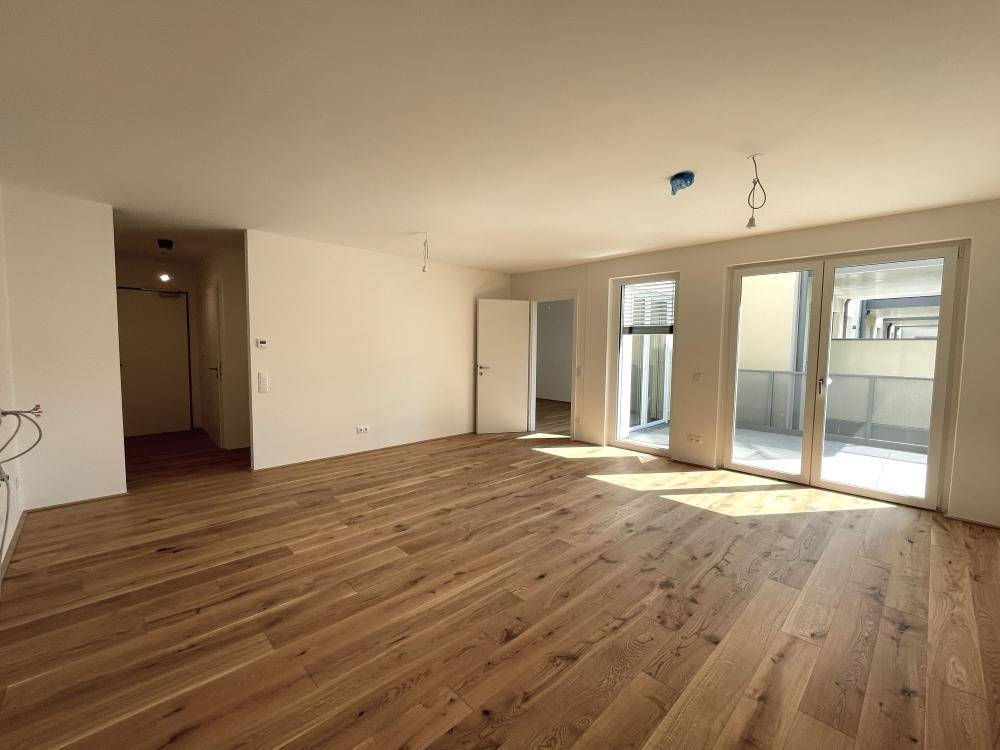 Großzügiger, heller Wohnbereich mit neuem Holzparkettboden und Zugang zum Balkon.