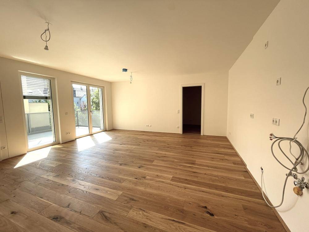 Lichtdurchfluteter Wohnbereich mit hochwertigem Holzparkett und großen Fenstern zum Außenbereich.