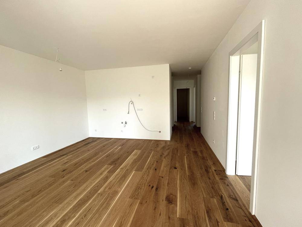 Langer, heller Raum mit neuem Holzparkettboden, vorbereitet für die Installation einer Küche oder Wohnbereich.
